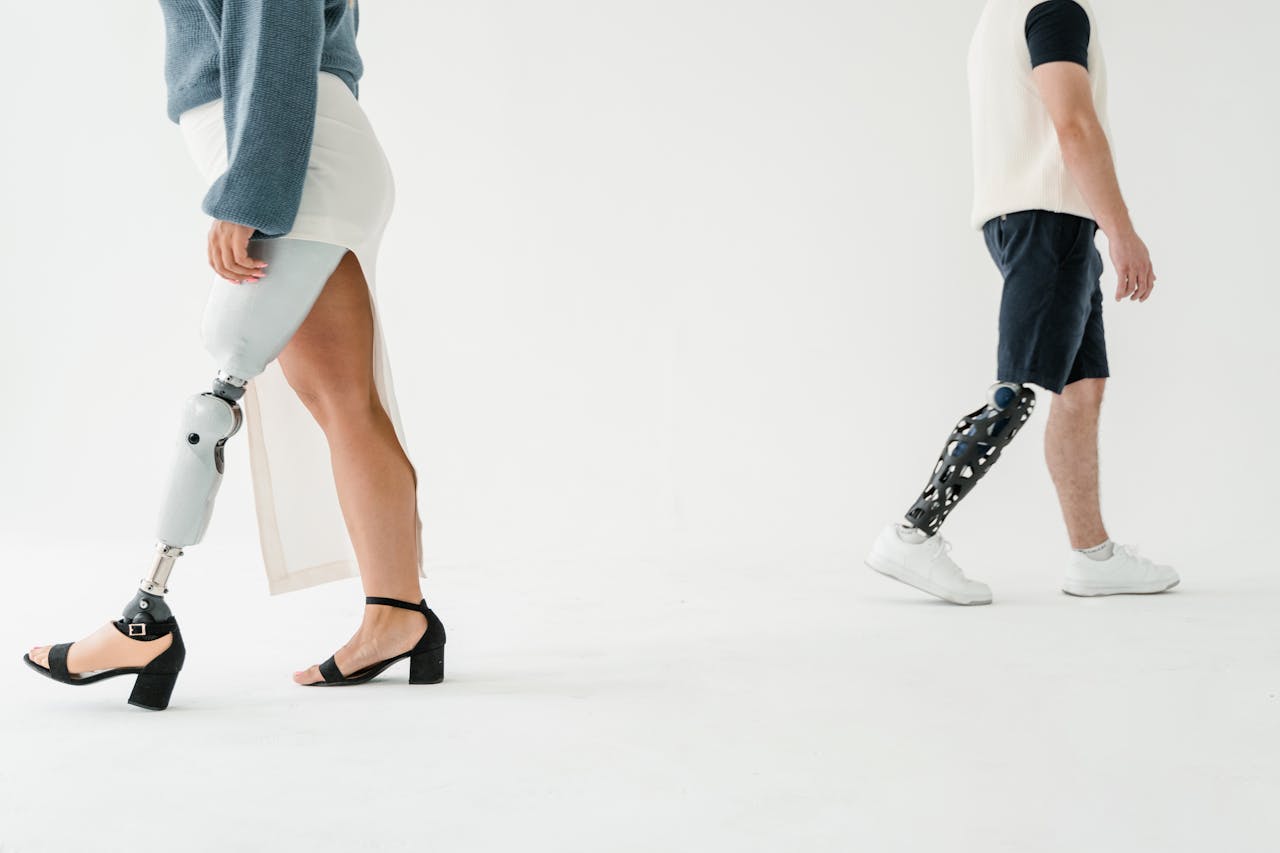 Two individuals with prosthetic legs walking in a studio, highlighting modern prosthetic technology.