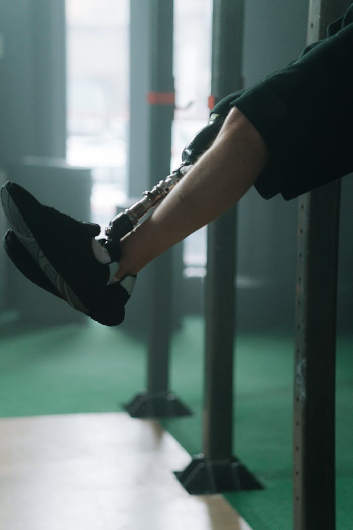 Close-up of prosthetic leg and black shoes in gym environment.